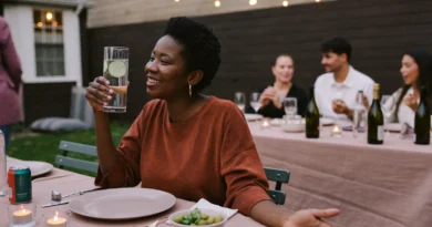 Smiling woman holding a glass of sparkling water with cucumber at a backyard dinner party under string lights