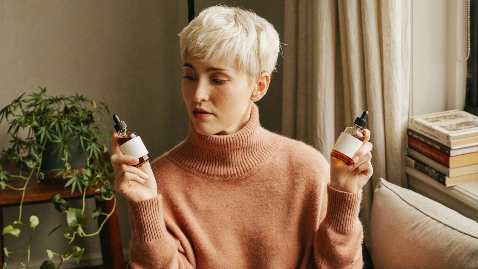 Woman with a short platinum pixie cut comparing two small amber dropper bottles by a sunny window