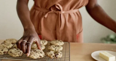 Mom in a rust apron placing homemade chocolate chip cookies on a cooling rack next to a dish of butter while making edibles at home