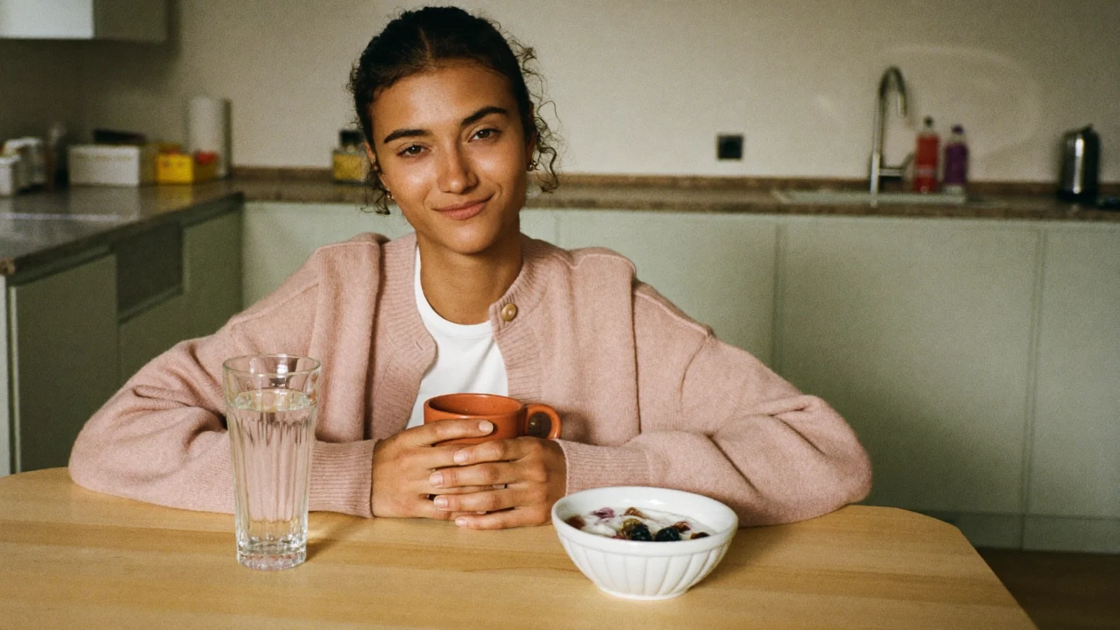 Sleepy mom at the kitchen table in the morning with a mug, a glass of water and a bowl of yogurt, easing through a THC hangover