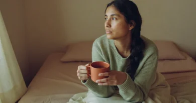 Tired but calm mom in a sage sweater sitting on the edge of her bed in the morning with a mug of herbal tea during a break from THC