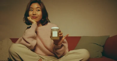 Mom in a blush sweater on a terracotta sofa holding a small jar with a puzzled smile, wondering why her edibles are not working